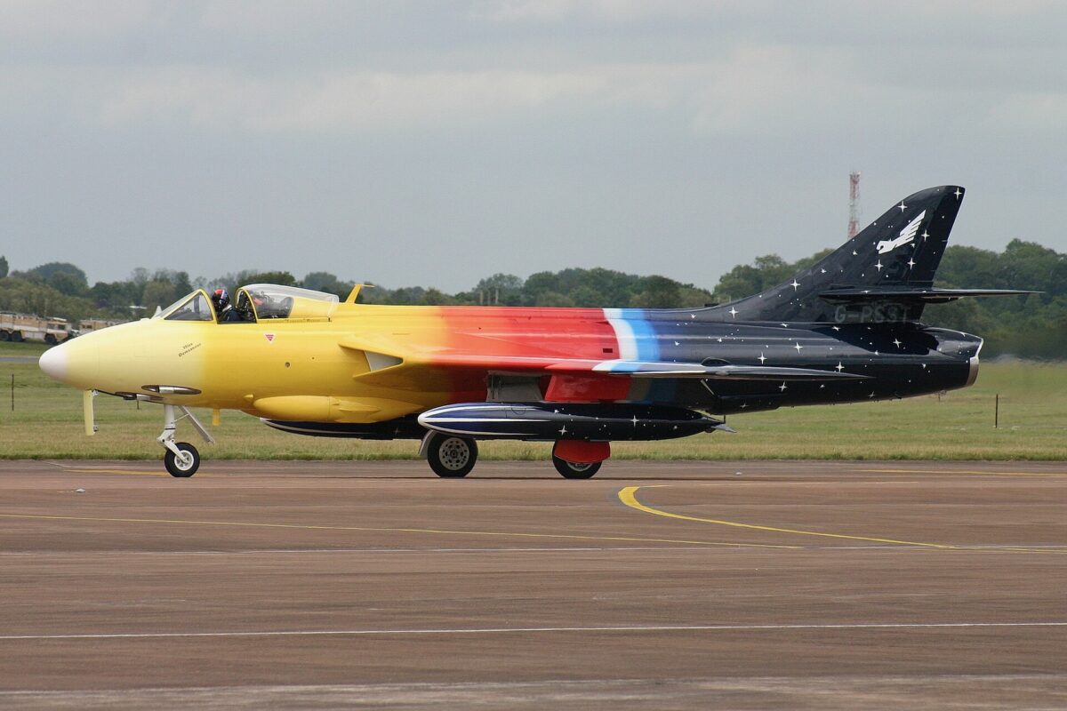 Recently Saved 1 of 1 15 Side view of a colorful aerobatic jet on a taxiway yellow nose rainbow gradient along the fuselage and a starry dark tail with a white emblem