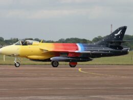 Side view of a colorful aerobatic jet on a taxiway yellow nose rainbow gradient along the fuselage and a starry dark tail with a white emblem