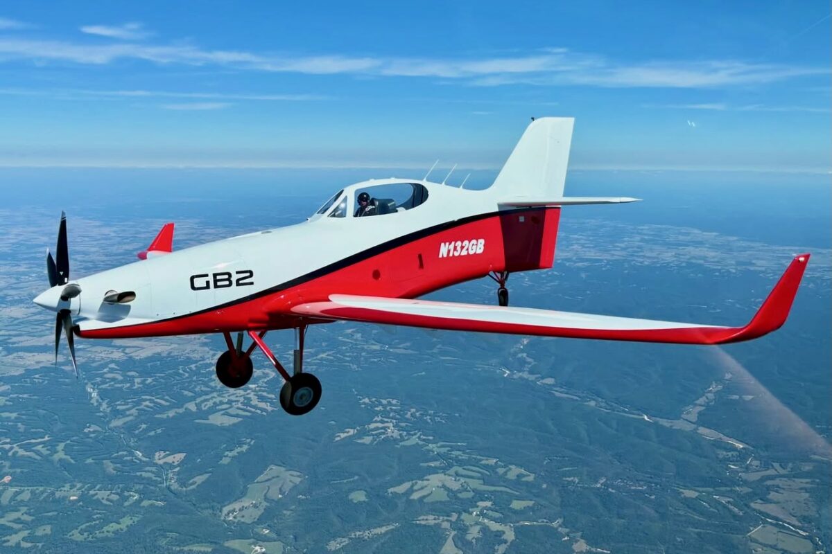Small red and white single engine aircraft in flight over countryside propeller blurred from speed cockpit visible with pilot inside
