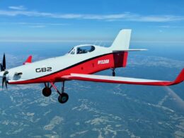 Small red and white single engine aircraft in flight over countryside propeller blurred from speed cockpit visible with pilot inside