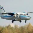 Twin turboprop airplane with landing gear down approaching runway over a treed landscape white with blue stripes and Russian flag on tail