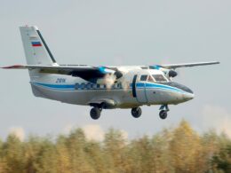 Twin turboprop airplane with landing gear down approaching runway over a treed landscape white with blue stripes and Russian flag on tail