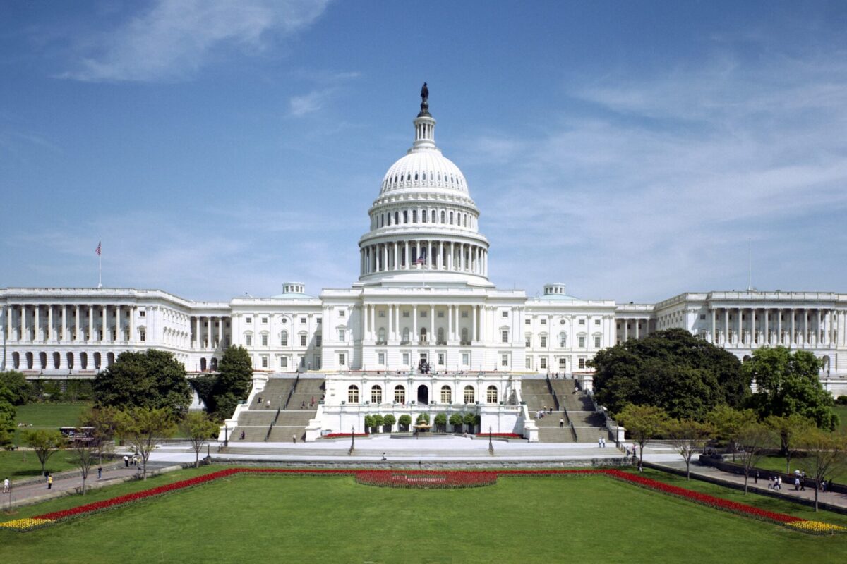 Front view of the US Capitol with its large central dome wings on both sides and a manicured lawn in the foreground