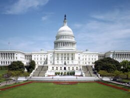 Front view of the US Capitol with its large central dome wings on both sides and a manicured lawn in the foreground