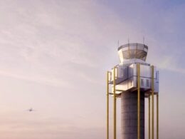 Air traffic control tower with bright yellow columns supporting a glass walled top a distant airplane in a pink blue sky
