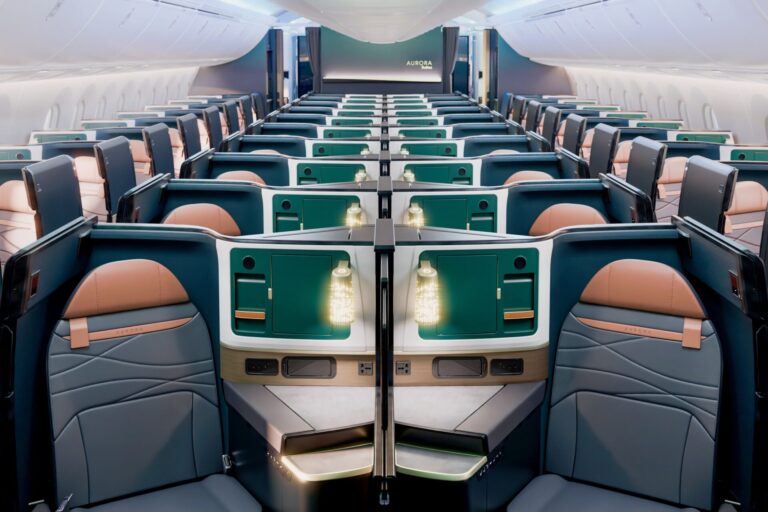 Wide view of a modern airplane cabin with private business class suites teal storage panels and peach seats along a long aisle
