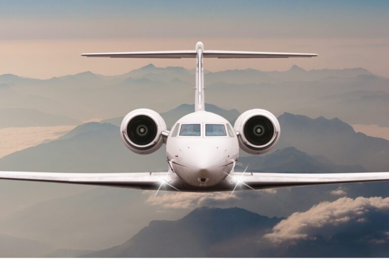 Front on view of a white passenger jet approaching the camera with mountains and clouds in the background during flight