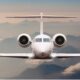 Front on view of a white passenger jet approaching the camera with mountains and clouds in the background during flight