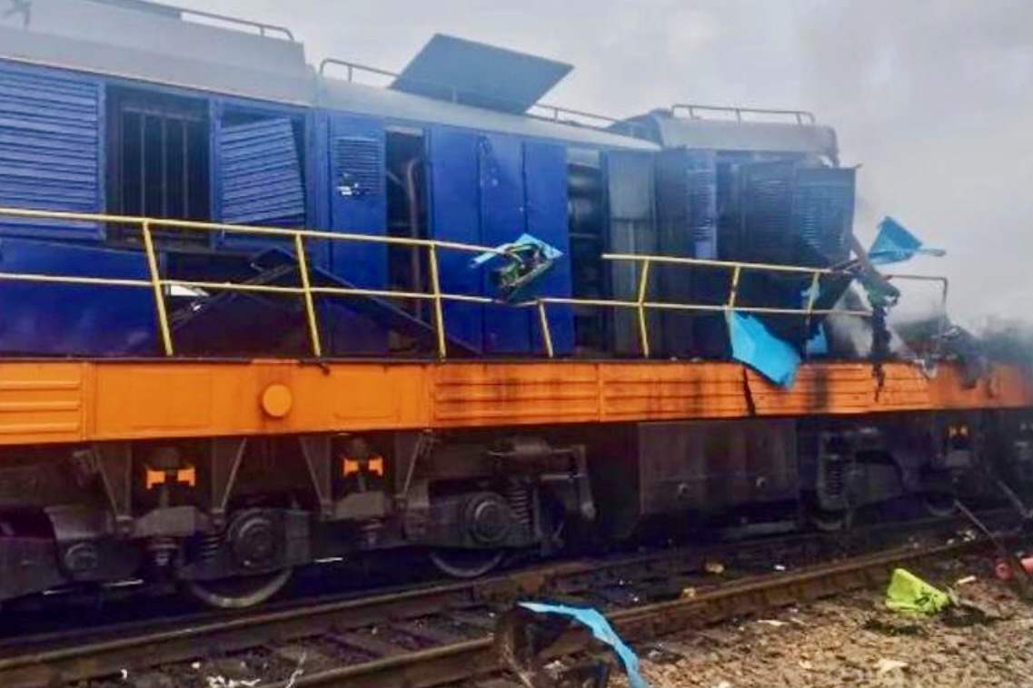 Recently Saved 1 of 1 6 Blue locomotive on an orange railcar appears damaged and derailed with scattered debris along the tracks in a cloudy scene