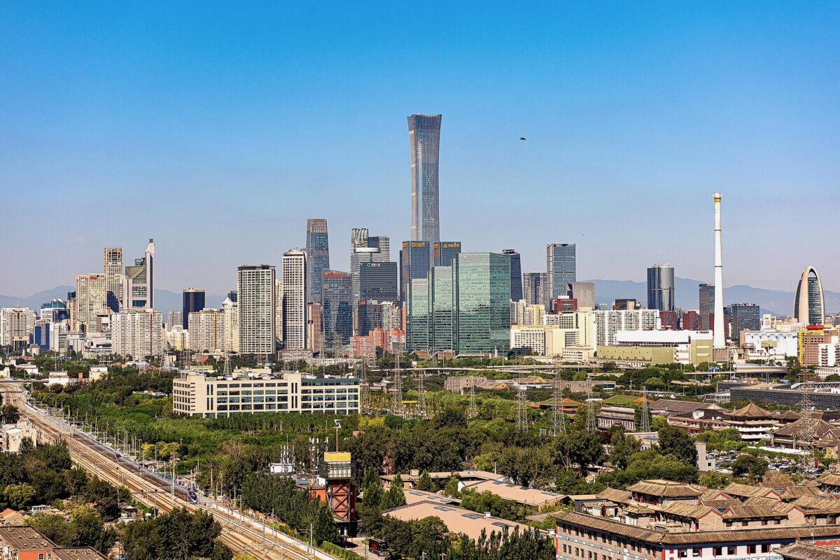 CBD City skyline with a tall glass skyscraper at center against a clear blue sky lower buildings and greenery in the foreground with mountains in the distance