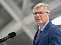 Man in a blue suit and pink tie speaking into a microphone