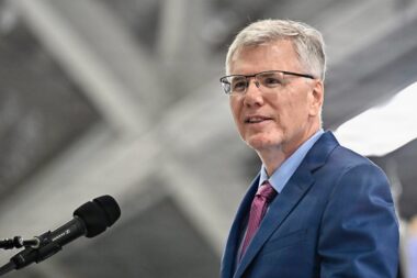 Man in a blue suit and pink tie speaking into a microphone