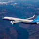 Boeing 737 MAX in blue and white livery flying over a rugged mountain range beneath a clear sky