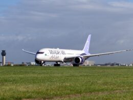 Riyadh Air widebody airplane taxiing on a runway with a purple tailed livery and a control tower in the distance