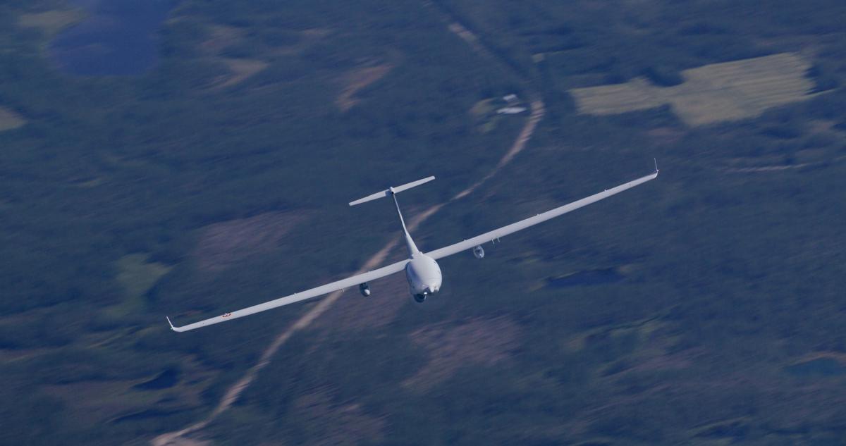 Safran Patroller tactical drone during a test flight White glider flying toward the camera over a forested hilly landscape Wings are long and straight with slight wingtip fins visible
