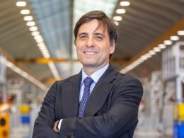 Professional man in a dark suit with arms crossed in a bright industrial warehouse