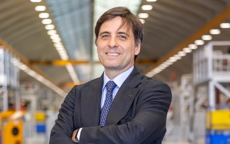 Professional man in a dark suit with arms crossed in a bright industrial warehouse