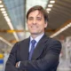 Professional man in a dark suit with arms crossed in a bright industrial warehouse