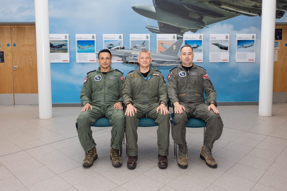 CON 20260908 633 TTF Turkish Pilots PR Three pilots in olivegreen flight suits sit on a bench in front of an aviation museum display of aircraft posters and a model jet behind them