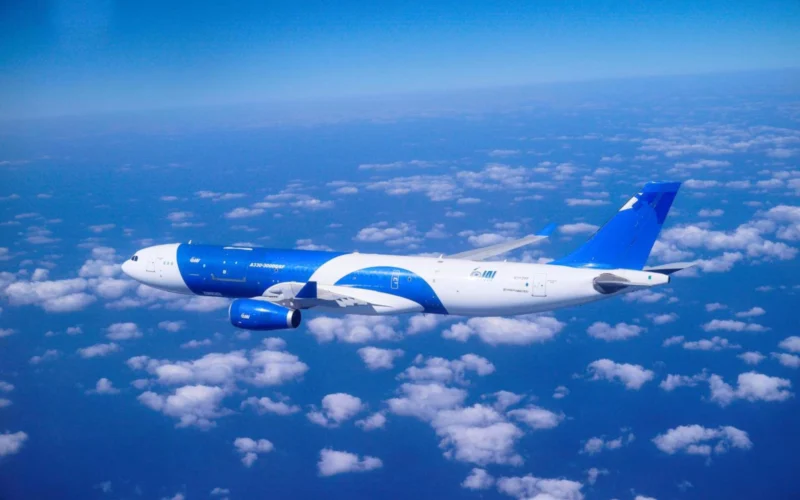 Blue and white commercial airplane cruising above a sea of clouds in a clear blue sky seen from the side of the fuselage and wing