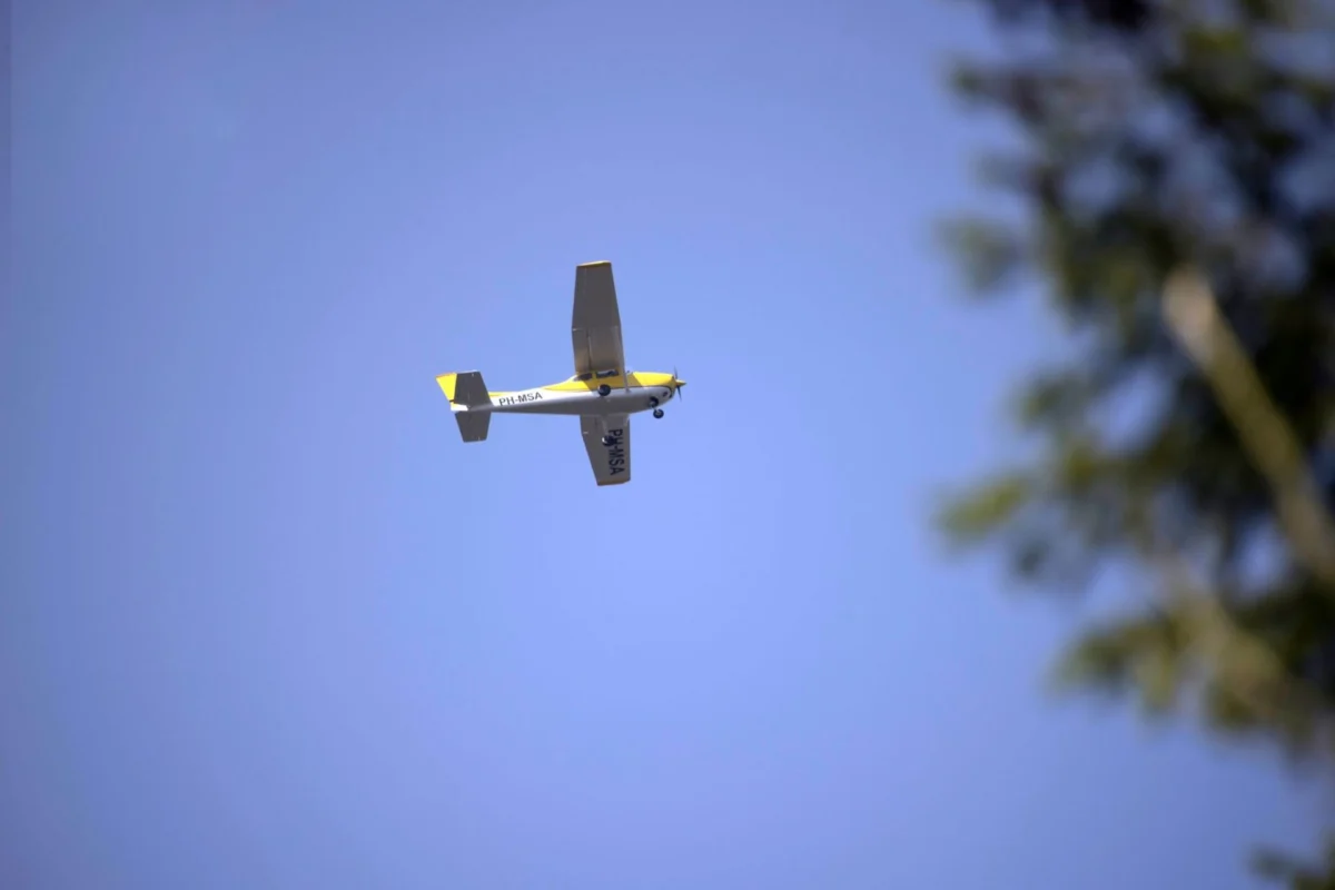 Two killed after Cessna crashes at San Diego airport Small yellow and white single engine airplane flying overhead in a clear blue sky with blurred tree on the right