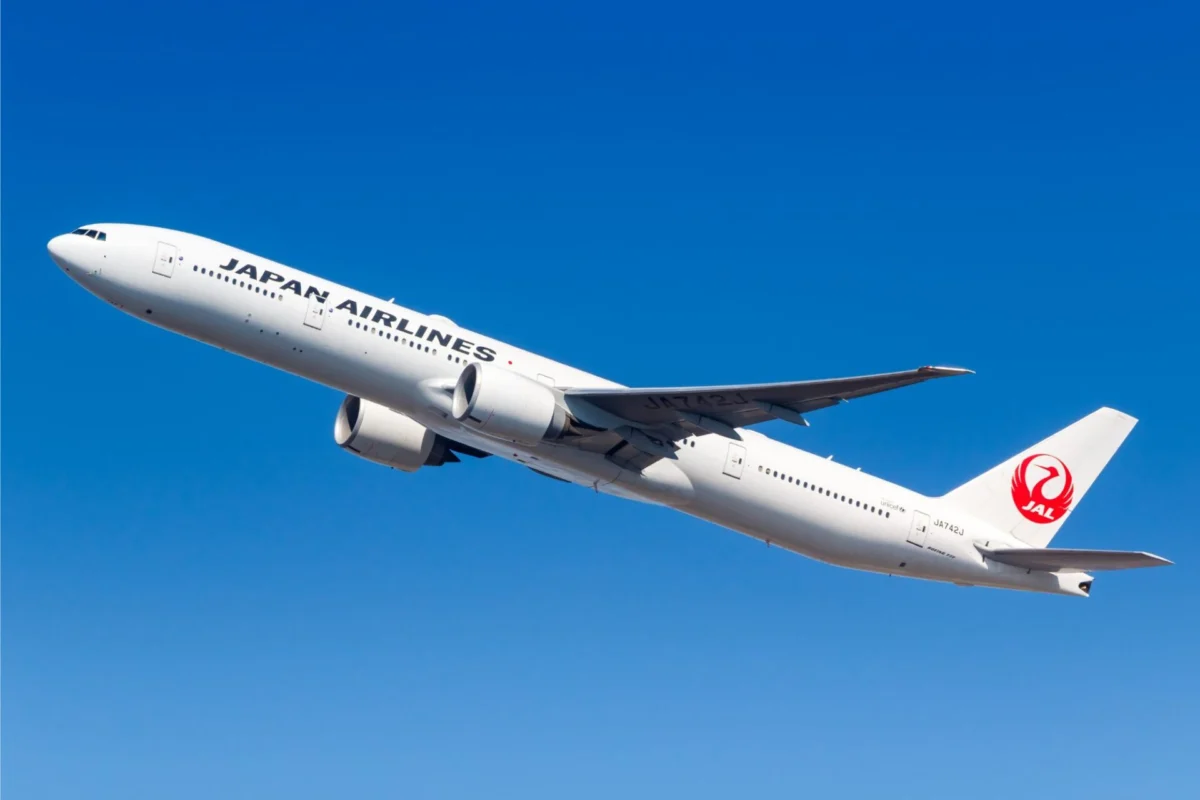 White Japan Airlines jet in flight against a clear blue sky with the red crane logo on the tail