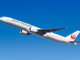 White Japan Airlines jet in flight against a clear blue sky with the red crane logo on the tail