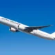 White Japan Airlines jet in flight against a clear blue sky with the red crane logo on the tail
