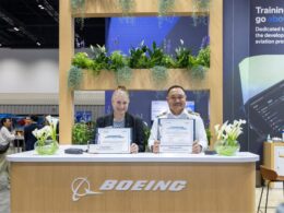 Two professionals at a Boeing exhibition booth display commemorative certificates among greenery