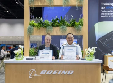 Two professionals at a Boeing exhibition booth display commemorative certificates among greenery.