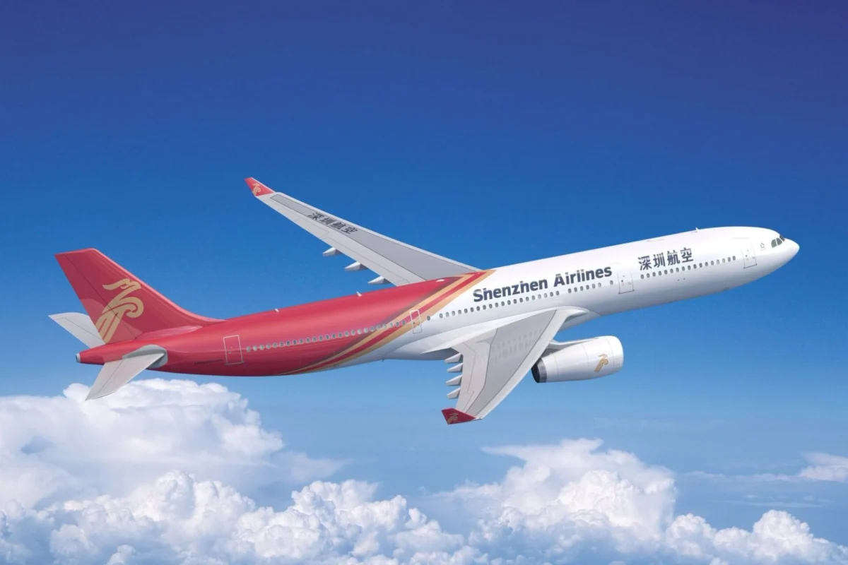Shenzhen Airlines passenger jet flying high above white clouds with a clear blue sky