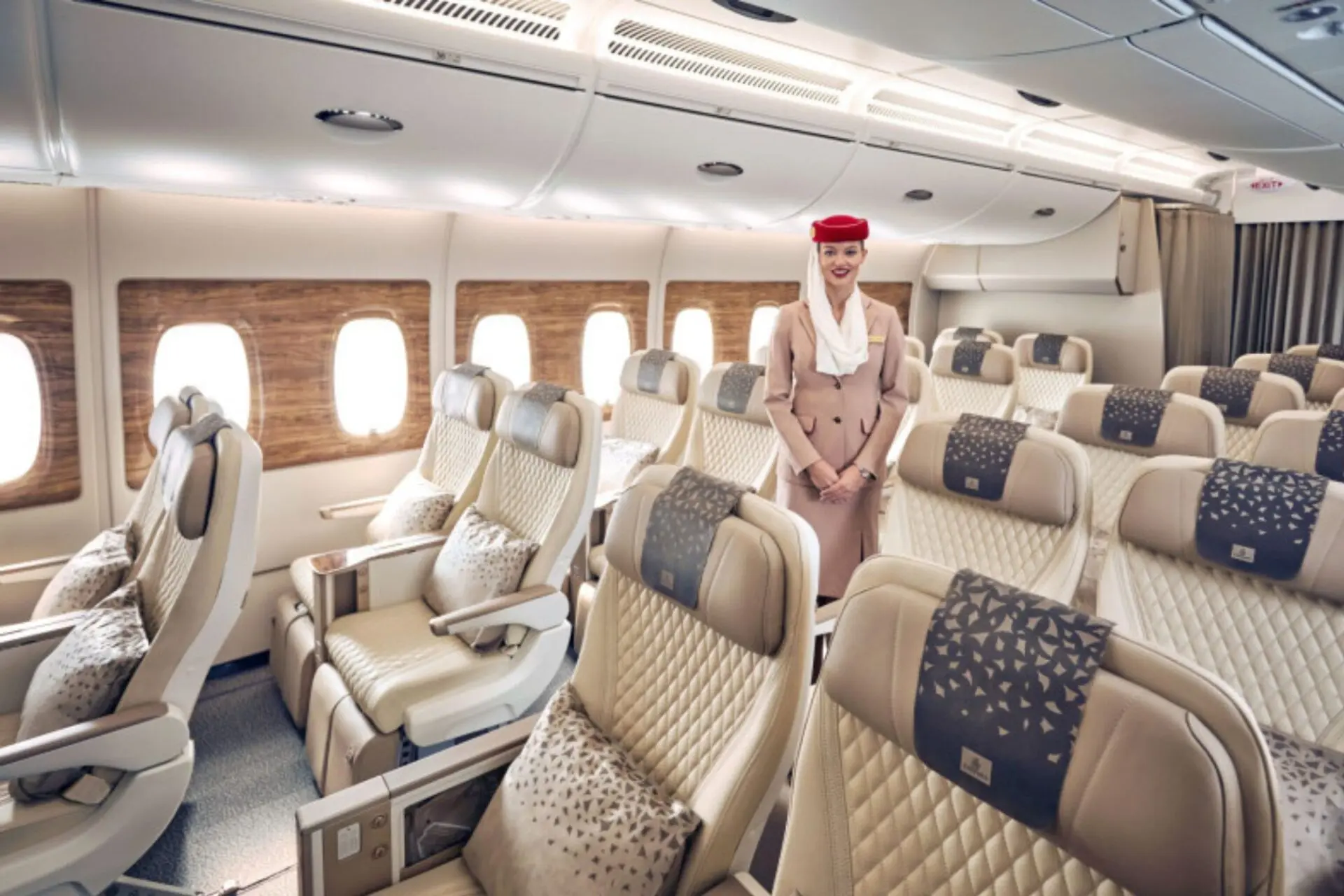 Flight attendant in beige uniform standing in a spacious passenger cabin with beige quilted seats and wood patterned window panels