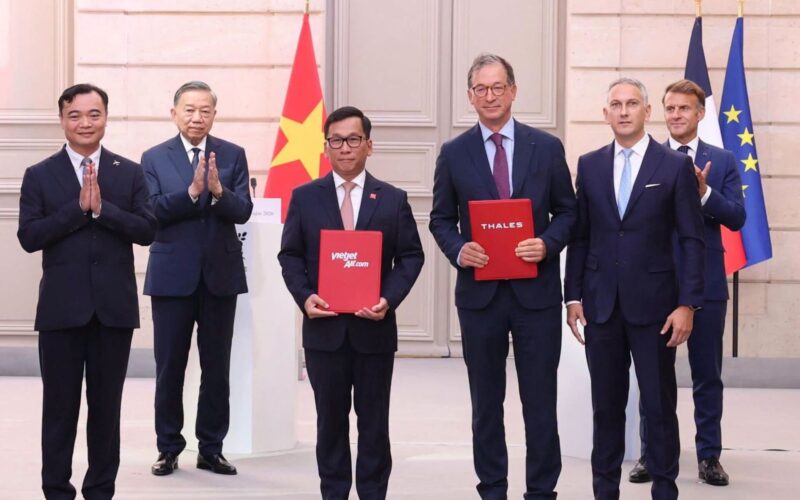 Vietjet and Thales sign major MRO and AI deals in Paris Six men in suits stand on a stage with flags in the background two hold red folders labeled vietjetaircom and THALES