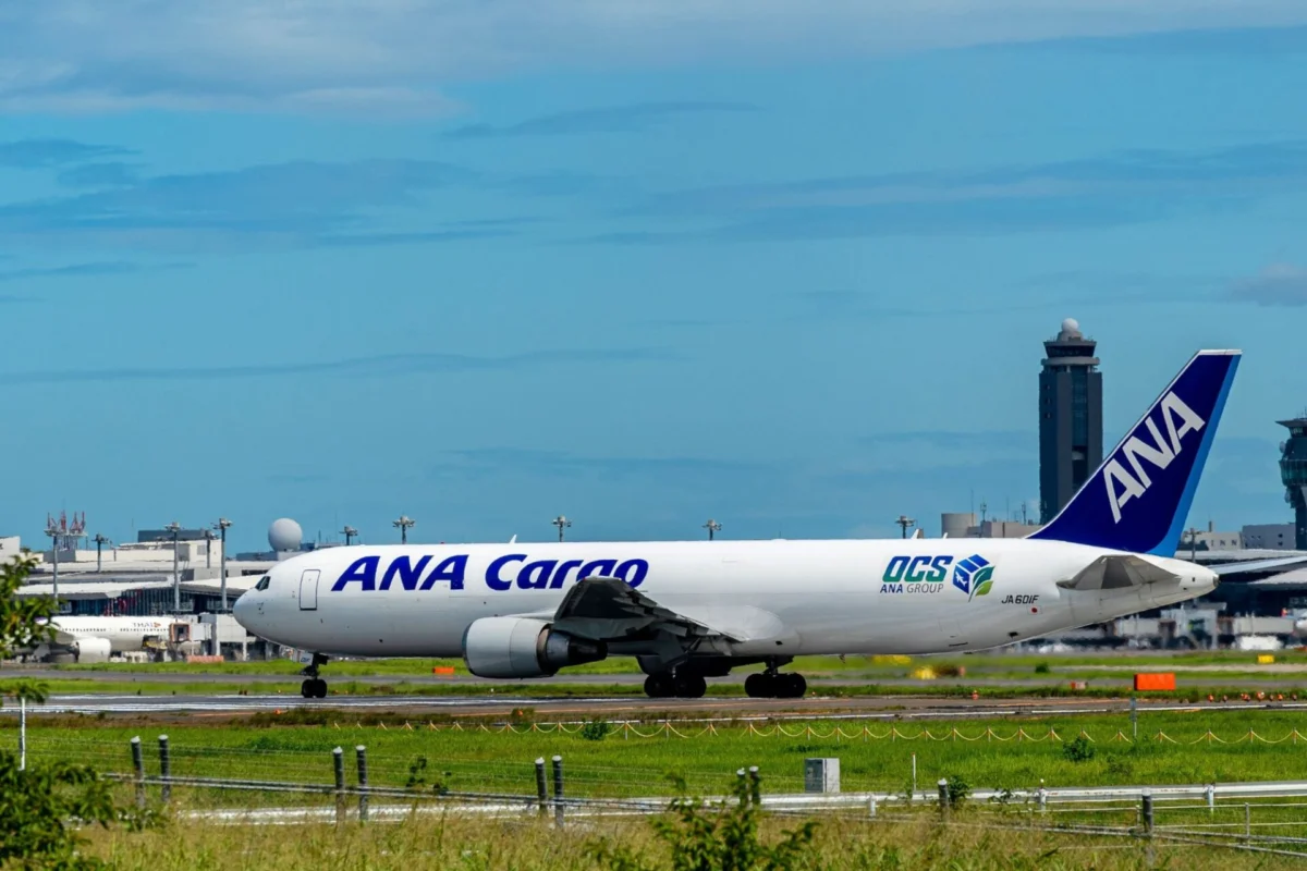 ANA Holdings names new cargo airline ANA Nippon Cargo Airliner with ANA Cargo livery on the taxiway at a sunny airport with blue sky and control tower in the background