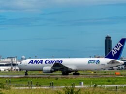Airliner with ANA Cargo livery on the taxiway at a sunny airport with blue sky and control tower in the background