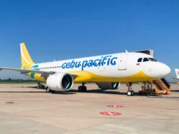 Cebu Pacific passenger jet on the tarmac beside a jet bridge under a clear blue sky