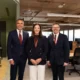Three professionally dressed colleagues pose for a group photo in a modern office lobby