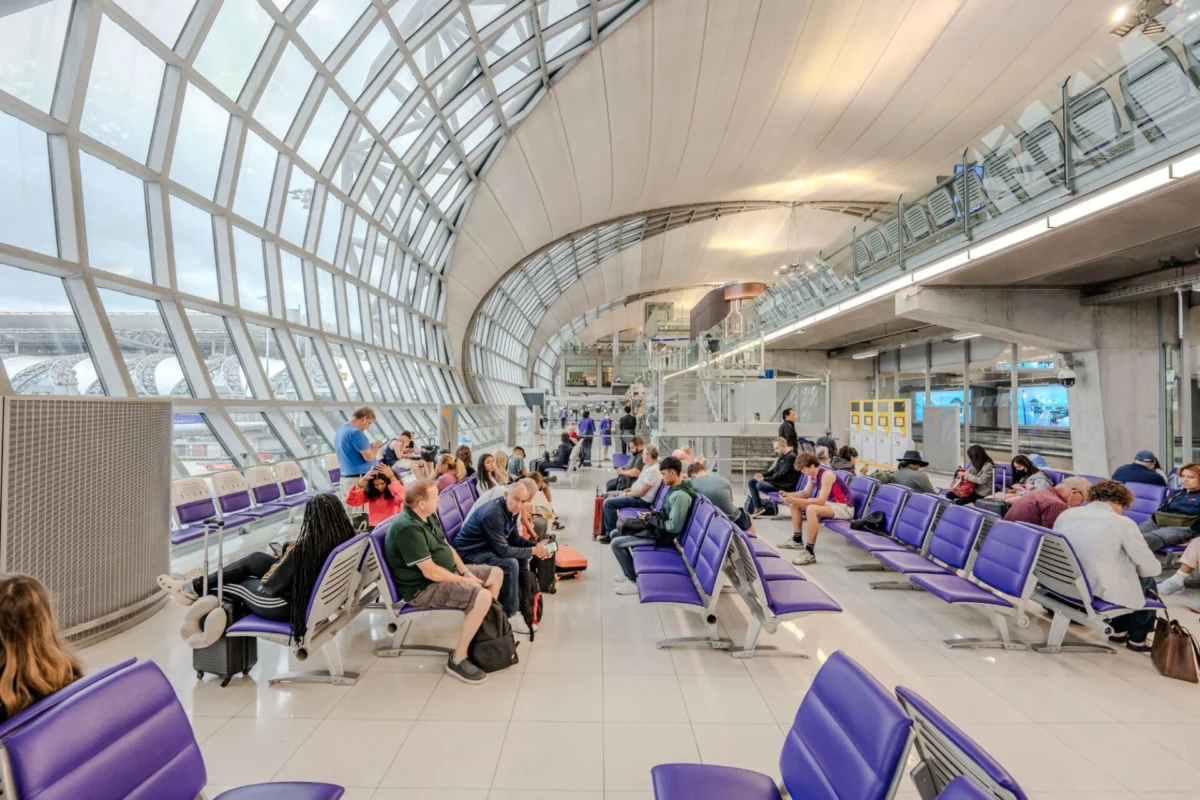 Bright airport waiting area with purple seats glass arched ceiling and travelers resting with luggage nearby