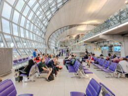 Bright airport waiting area with purple seats glass arched ceiling and travelers resting with luggage nearby
