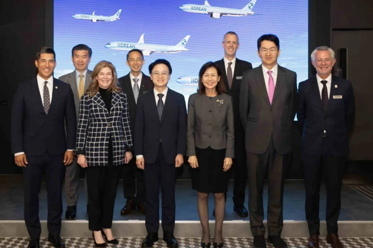 Korean Air seals US8B deal for Boeing jets GE engines Eight professionals in formal attire posing on a stage in front of a blue screen with airplanes at a corporate event