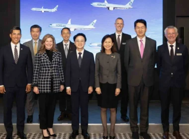 Eight professionals in formal attire posing on a stage in front of a blue screen with airplanes, at a corporate event.