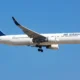 Air Astana passenger plane with landing gear down flying over a clear blue sky