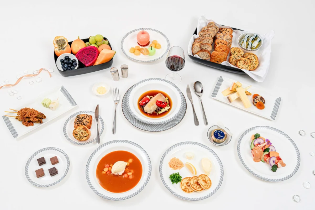 Singapore Airlines revamps in flight dining with 100 dishes Top down view of a formal dining table with assorted dishes breads fruits and desserts on white plates and tablecloth
