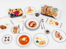 Top down view of a formal dining table with assorted dishes breads fruits and desserts on white plates and tablecloth