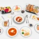 Top down view of a formal dining table with assorted dishes breads fruits and desserts on white plates and tablecloth