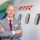 Executive in a gray suit and red striped tie stands with arms crossed beside an ATR aircraft in a hangar area