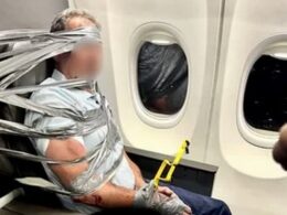 Person bound to an airplane seat with duct tape holding a yellow safety tool near the armrest beside a window