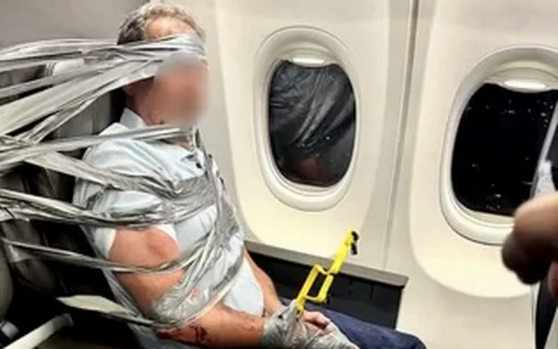 Person bound to an airplane seat with duct tape holding a yellow safety tool near the armrest beside a window