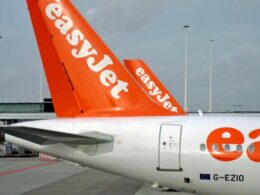 Rear of an EasyJet airplane with bright orange tail at the gate on the tarmac showing the logo and registration G EZIO