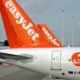 Rear of an EasyJet airplane with bright orange tail at the gate on the tarmac showing the logo and registration G EZIO